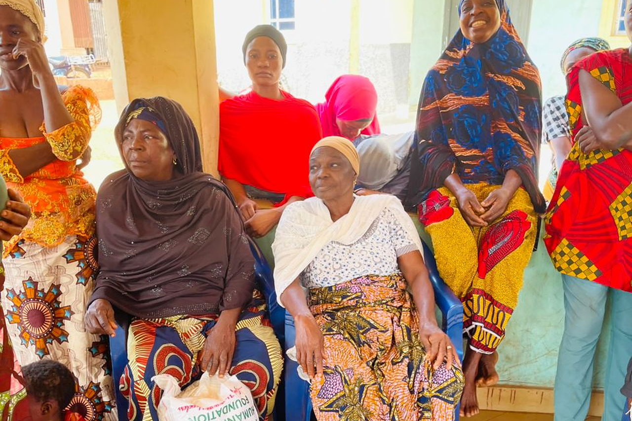 Women and children seated together during an Al Sa'eed Humanitarian Foundation food distribution, with relief bags beside them.