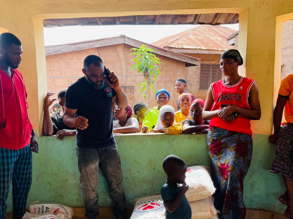 Families and children gathered at an Al Sa'eed Humanitarian Foundation distribution, with bags of supplies ready on the floor.