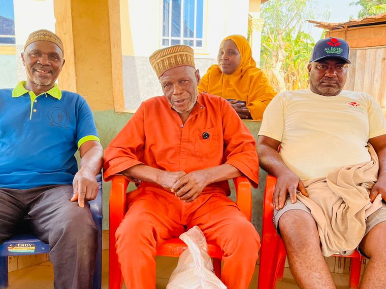 Three older men seated together, one with a bag of food supplies received from the Foundation.