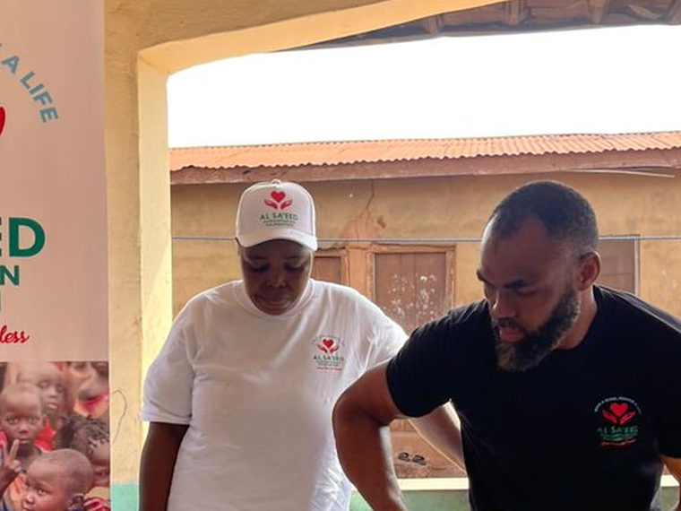 Two Al Sa'eed Humanitarian Foundation volunteers in branded uniform preparing relief bags.