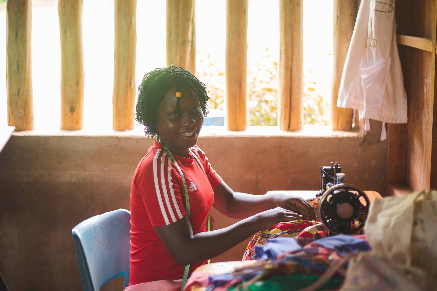 A young woman smiling as she works at a sewing machine in a community workshop.